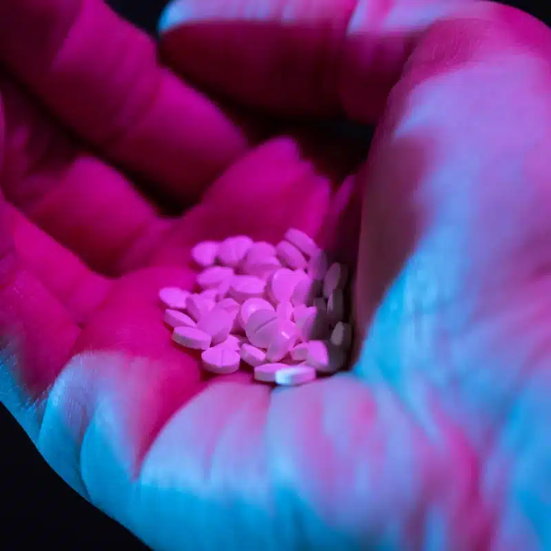 How Long Does Molly Last? A hand under blue and purple lighting holding white pills.