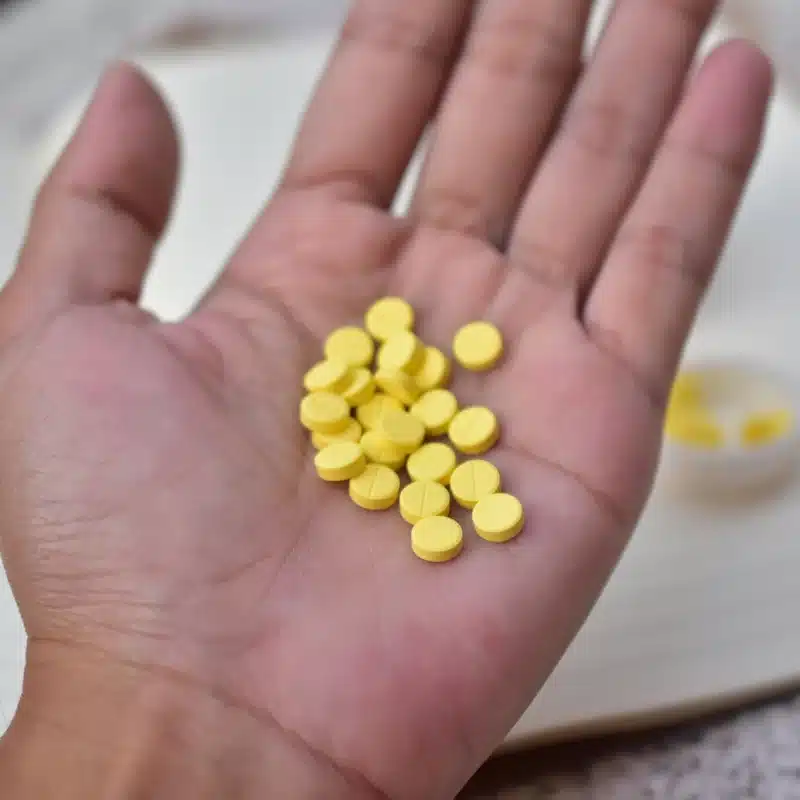How Long Does Percocet Stay In Your System? A hand holding a lot of yellow pills.