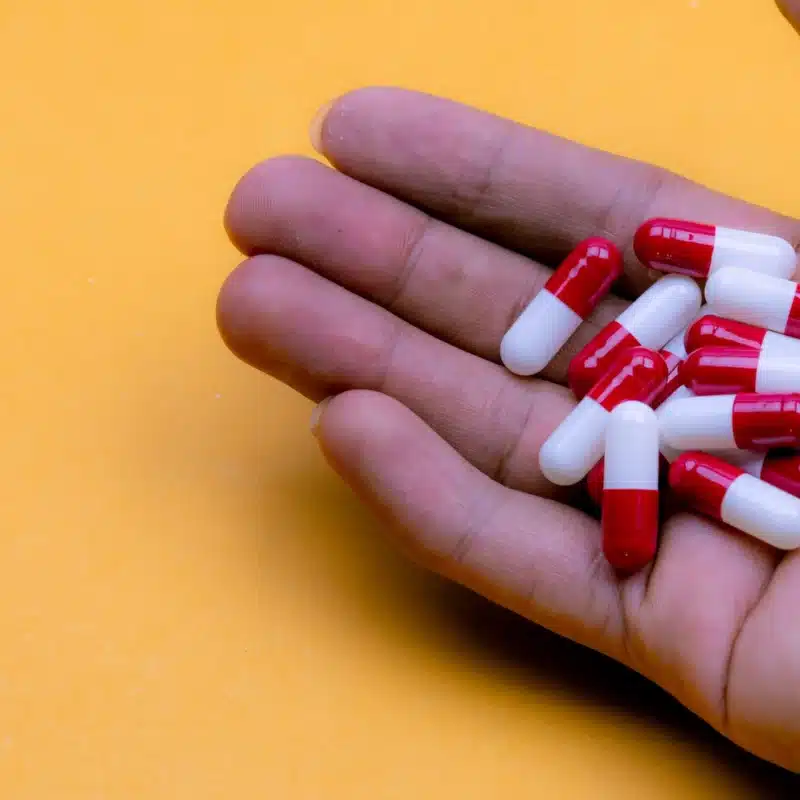 Is Lyrica a Controlled Substance? A hand holding red and white pill capsules over a yellow background.