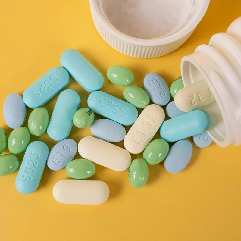 Variations of Adderall pills spilling out of a pill bottle on a table.